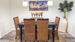 A dining area with a dark wooden table, woven chairs, and a painting of a beach scene. - 8th At The Bay, New Listing (Port St. Joe)