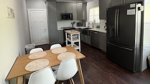 Una cocina moderna con armarios grises, un refrigerador de acero inoxidable y una zona de comedor con mesa de madera y sillas blancas.