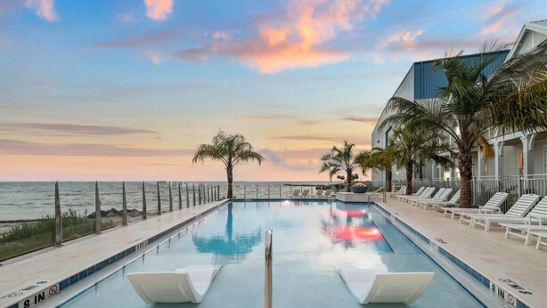 Ein Pool mit Sonnenuntergangsblick, Palmen und Liegestühlen am Pool.
