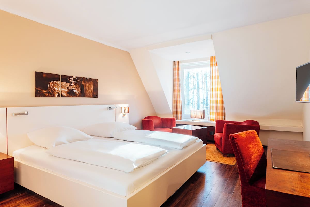 Ein Hotelzimmer mit einem großen Bett, zwei roten Sesseln, einem Holztisch und einem Bild an der Wand.