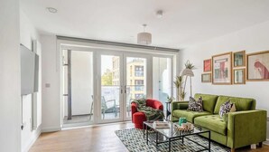 A modern living room with a green sofa, a red armchair, and a glass coffee table. There is a sliding glass door leading to an outdoor area. - Modern Apartment w/ Private Balcony, WiFi, Parking (Walton-on-Thames)