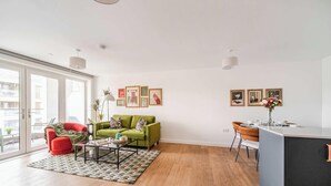Un salon moderne avec un canapé vert, un fauteuil rouge et une table basse en verre. On y trouve également un coin repas avec un bar et une vue dégagée grâce à de grandes fenêtres.