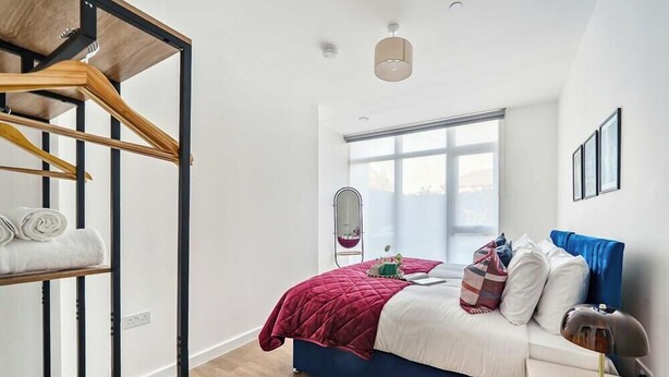 A bedroom with a bed, a wooden wardrobe, a mirror, and a window.