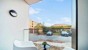 A balcony with a view of a parking area, a small table with a plant, and white chairs.