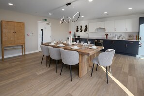 A modern kitchen with a central island, dark cabinets, and a wooden dining table set for six. - Modern 2BR Apartment w/ Balcony, Parking, WiFi (Walton-on-Thames)