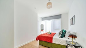 Quarto com cama verde, colcha acolchoada vermelha, mesa de cabeceira com abajur e janela com vista para o exterior.