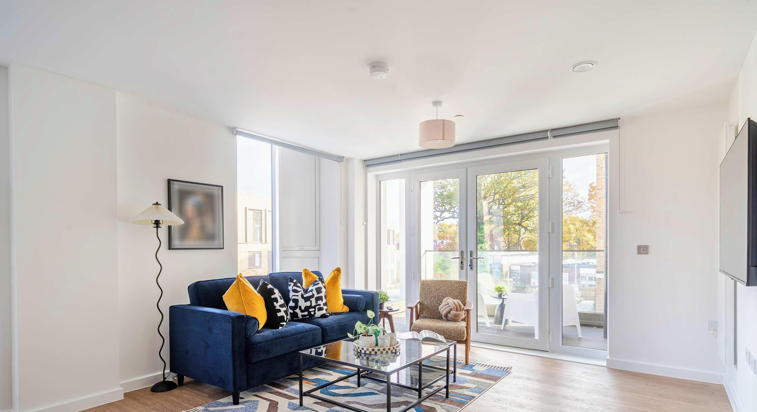 A modern living room with a blue sofa, a coffee table, and a large sliding glass door leading to an outdoor patio.