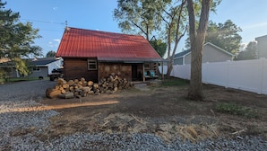Une cabane rustique avec un toit en métal rouge, une véranda en bois et une pile de bois de chauffage devant.