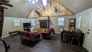 Un salon avec une cheminée, un téléviseur, un canapé, une table à manger avec des chaises et des murs en bois ornés de têtes d’animaux empaillées.