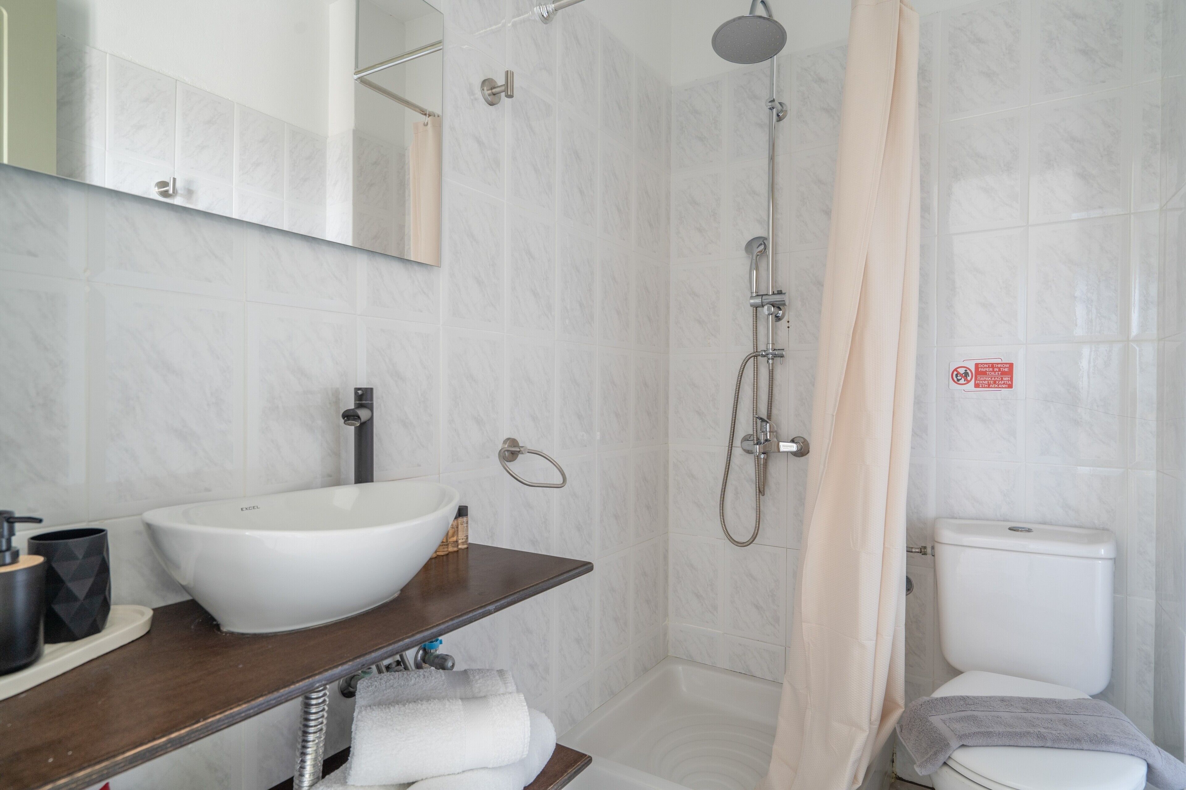 A bathroom with a white sink, a mirror, a shower, and a toilet.