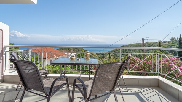 En balkon med et bord og stole, der udover et smukt udsigtspunkt over havet og grønne omgivelser.