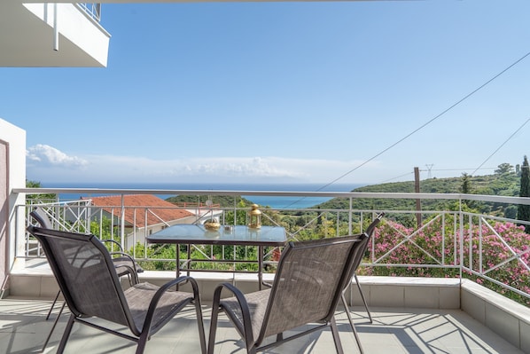 Ein Balkon mit Tisch und Stühlen, der einen schönen Blick auf das Meer und die grüne Landschaft bietet.