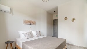 Et soveværelse med en seng, et lille bord, en vægmonteret aircondition og en dør.
