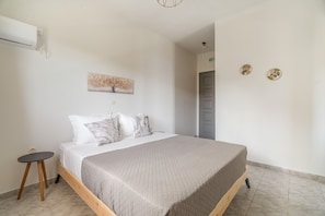 Ein Schlafzimmer mit einem Bett, einem kleinen Tisch, einer Wandklimaanlage und einer Tür.