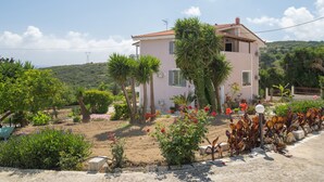 Une maison rose avec un toit en tuiles, entourée de verdure et sous un ciel dégagé.
