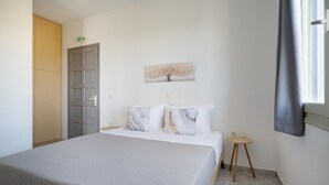 Une chambre d’hôtel avec un lit, une petite table d’appoint en bois, un tableau au mur et un panneau indiquant la sortie.