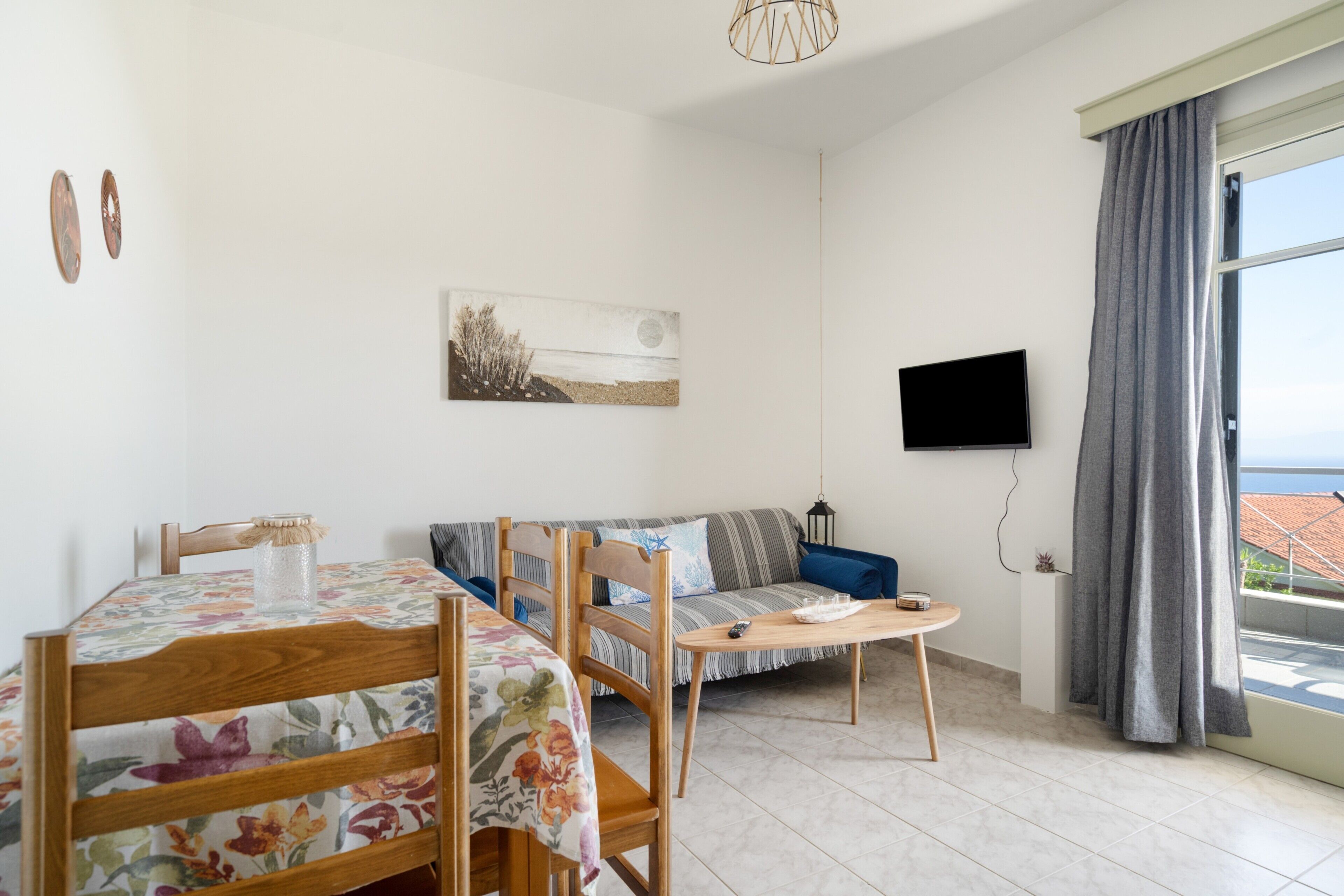 A room with a dining table, chairs, a sofa, a TV, and a window with curtains.