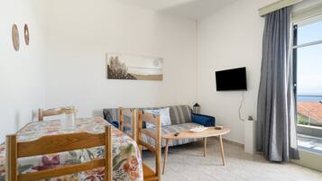 A room with a dining table, chairs, a sofa, a TV, and a window with curtains.