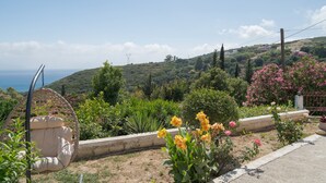 Un jardin avec un fauteuil suspendu, une variété de plantes et une vue sur des collines en arrière-plan.