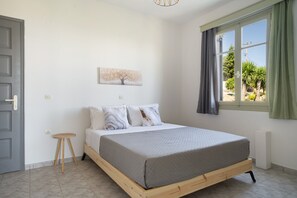 A bedroom with a bed, a small stool, a window with curtains, and a wall-mounted painting. - Apartment 'Maistrali First Floor  2' with Sea View, Wi-Fi and Air Conditioning (Ratzaklíon)