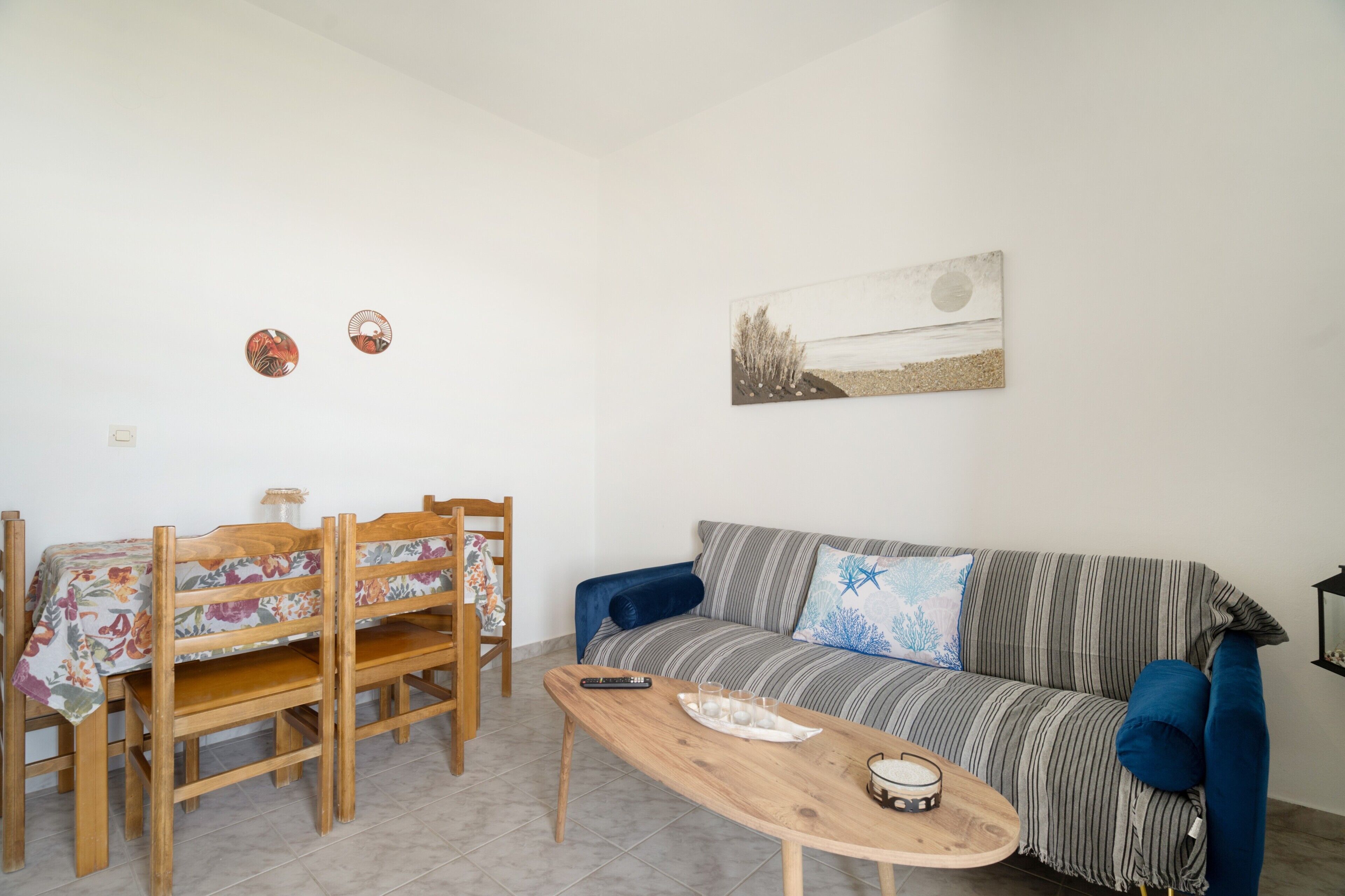A living room with a sofa, a coffee table, a dining table with chairs, and a wall art piece.