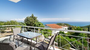 Un balcon avec une table et des chaises, donnant sur un paysage côtier avec des arbres et une vue sur la mer.