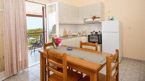 Una cocina con armarios blancos, una mesa de comedor con sillas, un refrigerador y vistas a través de una puerta de vidrio.