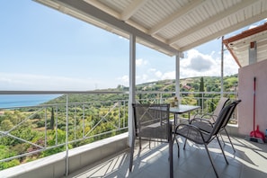 Een balkon met een tafel en stoelen, met uitzicht op een schilderachtig landschap met heuvels en een waterpartij.