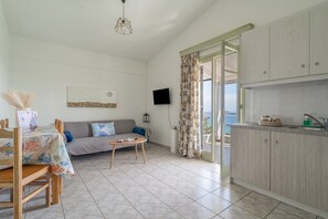 Een woonkamer met een bank, salontafel, eettafel en een keukenhoek met kastjes en een televisie.