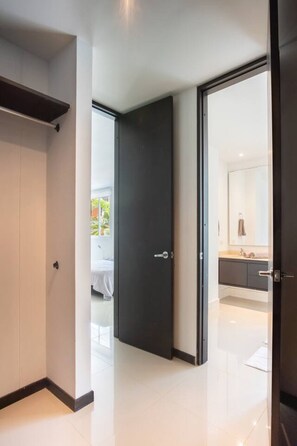 A modern hotel room with a large bed, a dark door, and a bathroom visible through an open door. - Light-filled Barranquilla apt with relaxing pool (Barranquilla)