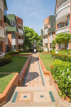 A courtyard with a central pathway flanked by brick buildings with balconies, surrounded by well-maintained greenery. - Light-filled Barranquilla apt with relaxing pool (Barranquilla)