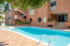 A swimming pool with a brick building in the background, a lifebuoy, and a staircase leading to an upper level. - Light-filled Barranquilla apt with relaxing pool (Barranquilla)