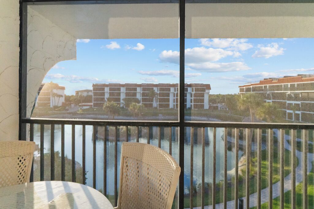 Een balkon met rieten stoelen en een tafel, met uitzicht op een waterpartij en gebouwen op de achtergrond.