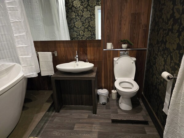 Une salle de bain avec une baignoire, un lavabo, des toilettes et une petite étagère sur laquelle est posée une plante en pot.