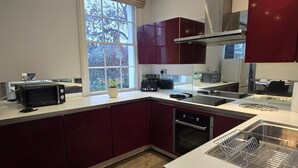 A modern kitchen with dark red cabinets, a built-in oven, a microwave, and a stainless steel range hood. - Apartment - Sleeps 6 & Near Station (Bedford)
