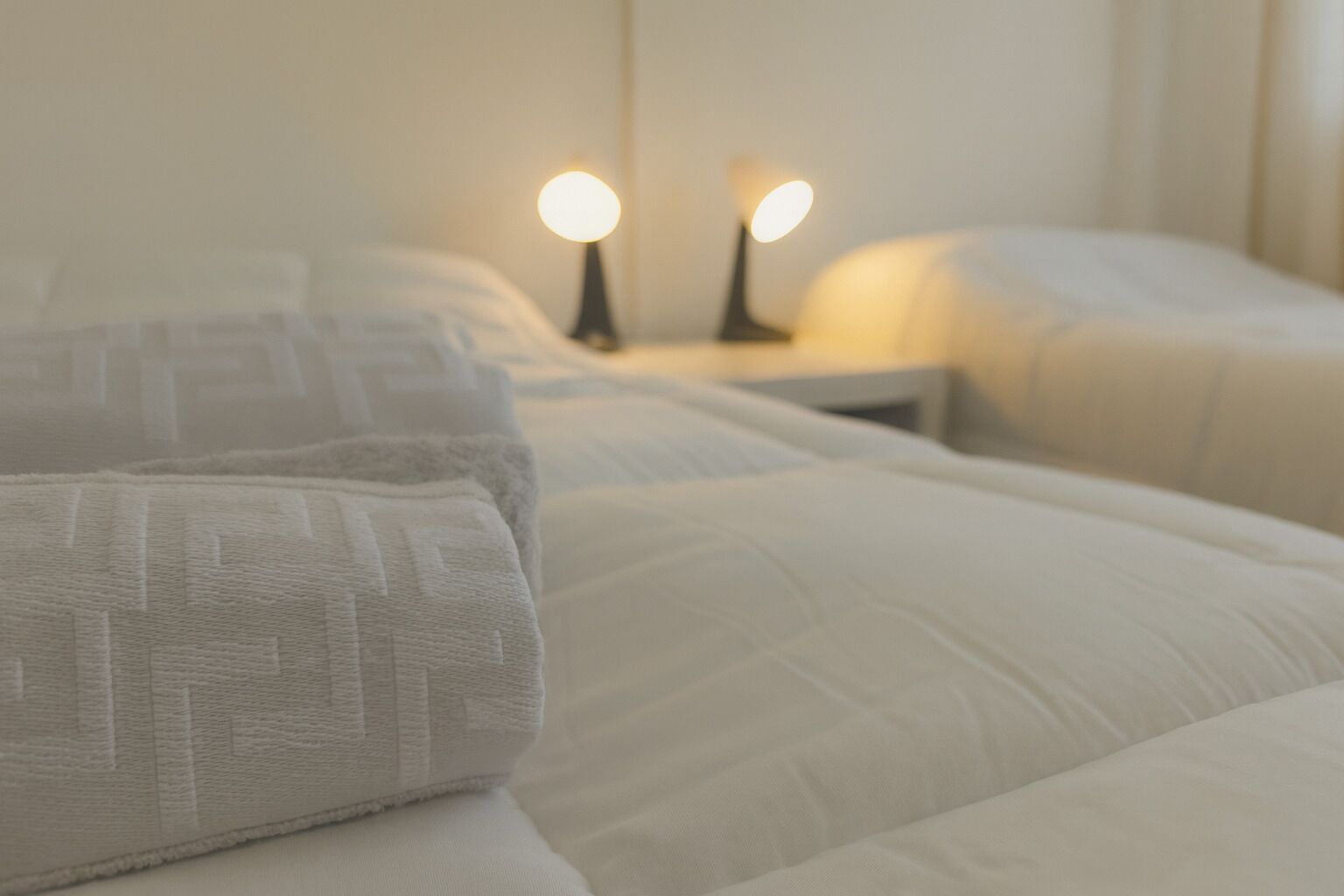 A neatly made bed with white linens and two bedside lamps.