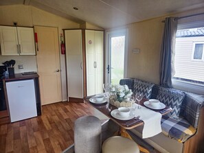 Cocina compacta con refrigerador, armarios y una zona de comedor con banco y mesa para dos.