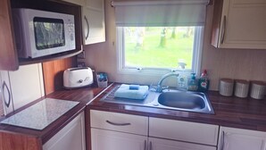 Eine kompakte Küchenzeile mit Mikrowelle, Toaster, Spüle und Fenster mit Blick auf Grünflächen.