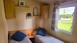 Ein gemütliches Schlafzimmer mit zwei Betten, einem Nachttisch mit Lampe und einem Fenster mit Blick auf eine grüne Rasenfläche.