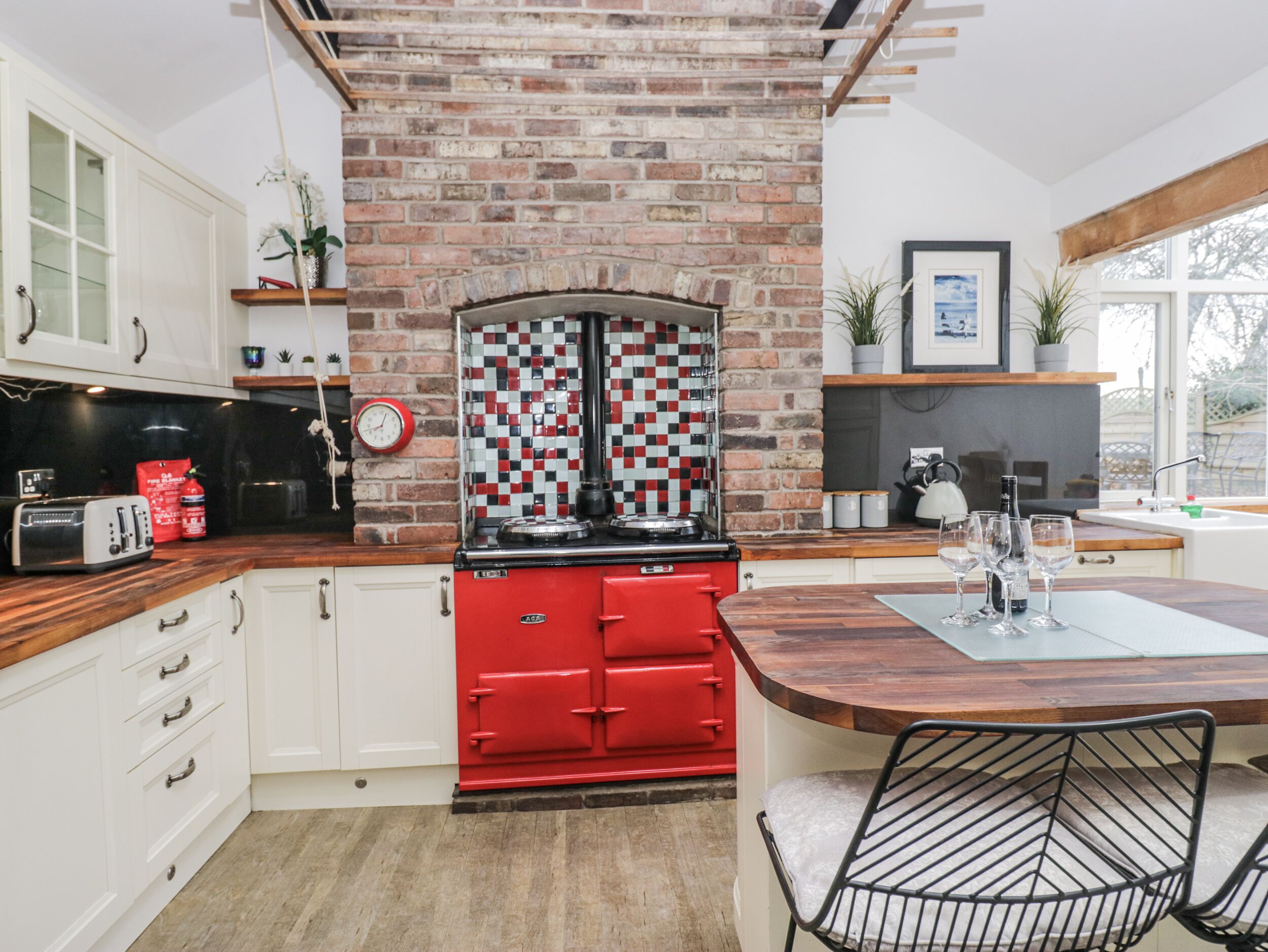 A kitchen with a brick wall, a red stove, white cabinets, and a wooden countertop.