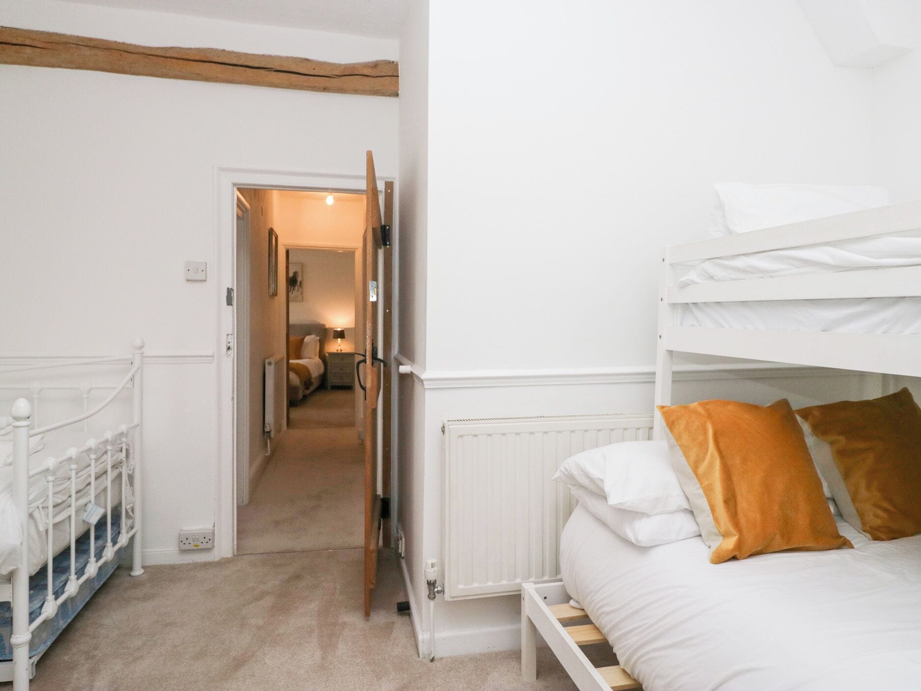 Une chambre avec des lits superposés, un radiateur blanc et un couloir menant à une autre pièce.