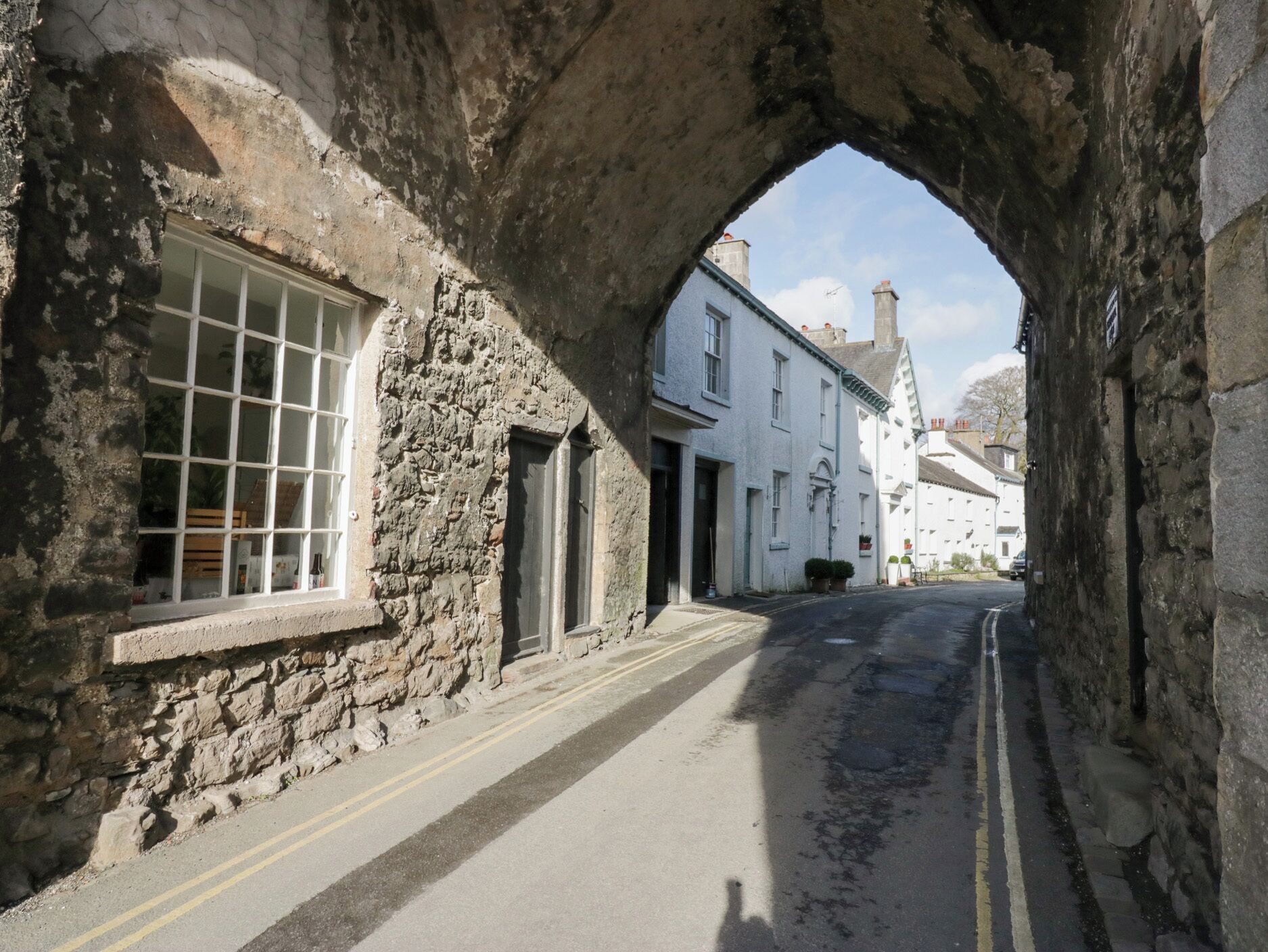 A narrow street with stone buildings, a clear sky, and a visible archway.