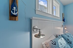 Ein Schlafzimmer mit einem weißen Bettkopfs, einer Pendelleuchte und einem Fenster mit Blick auf den Himmel.