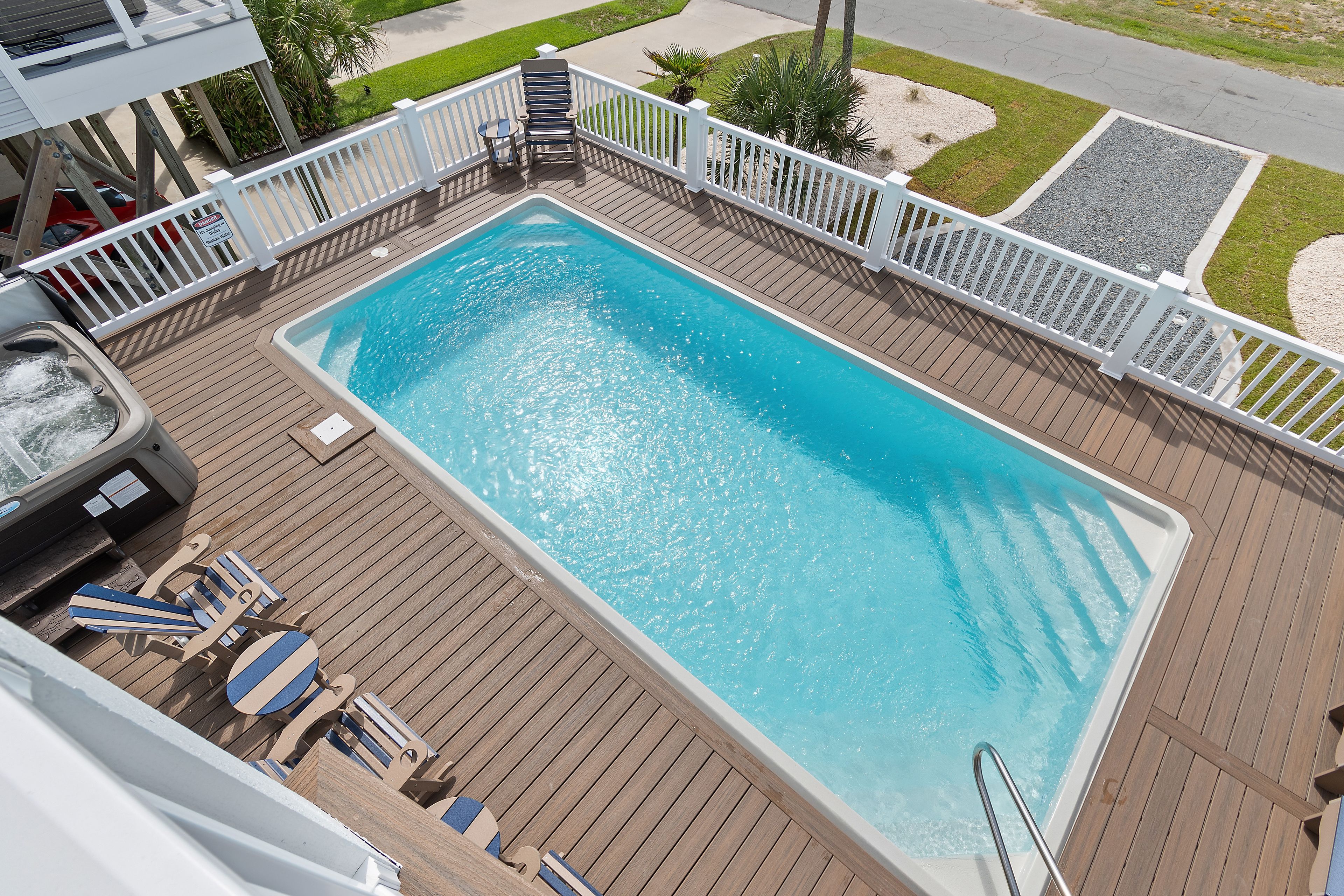 A rectangular swimming pool with a wooden deck surrounding it, a hot tub, and lounge chairs.