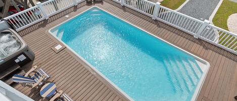 A rectangular swimming pool with a wooden deck surrounding it, a hot tub, and lounge chairs.
