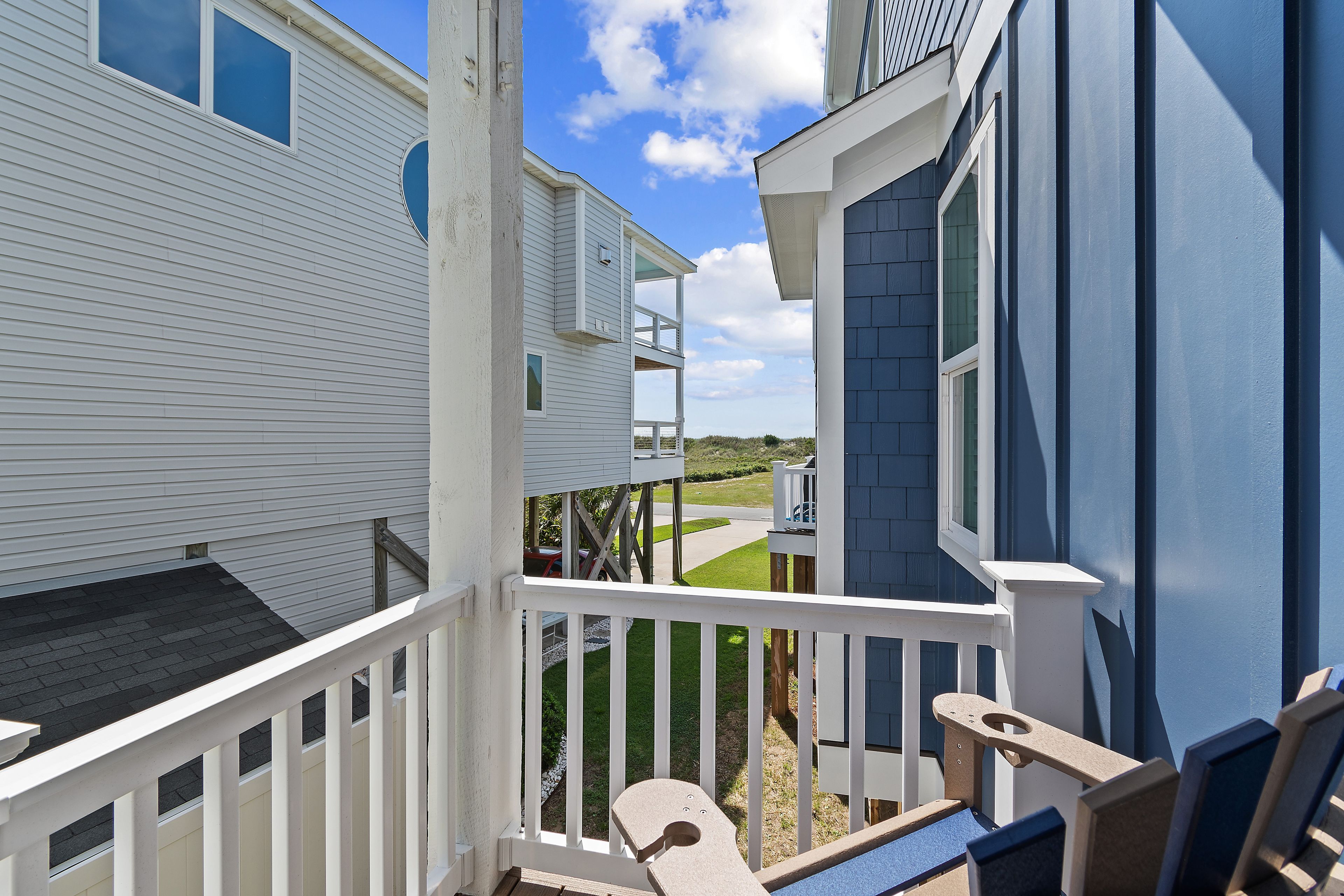 A residential building with a balcony, a clear sky, and a view of a green landscape.