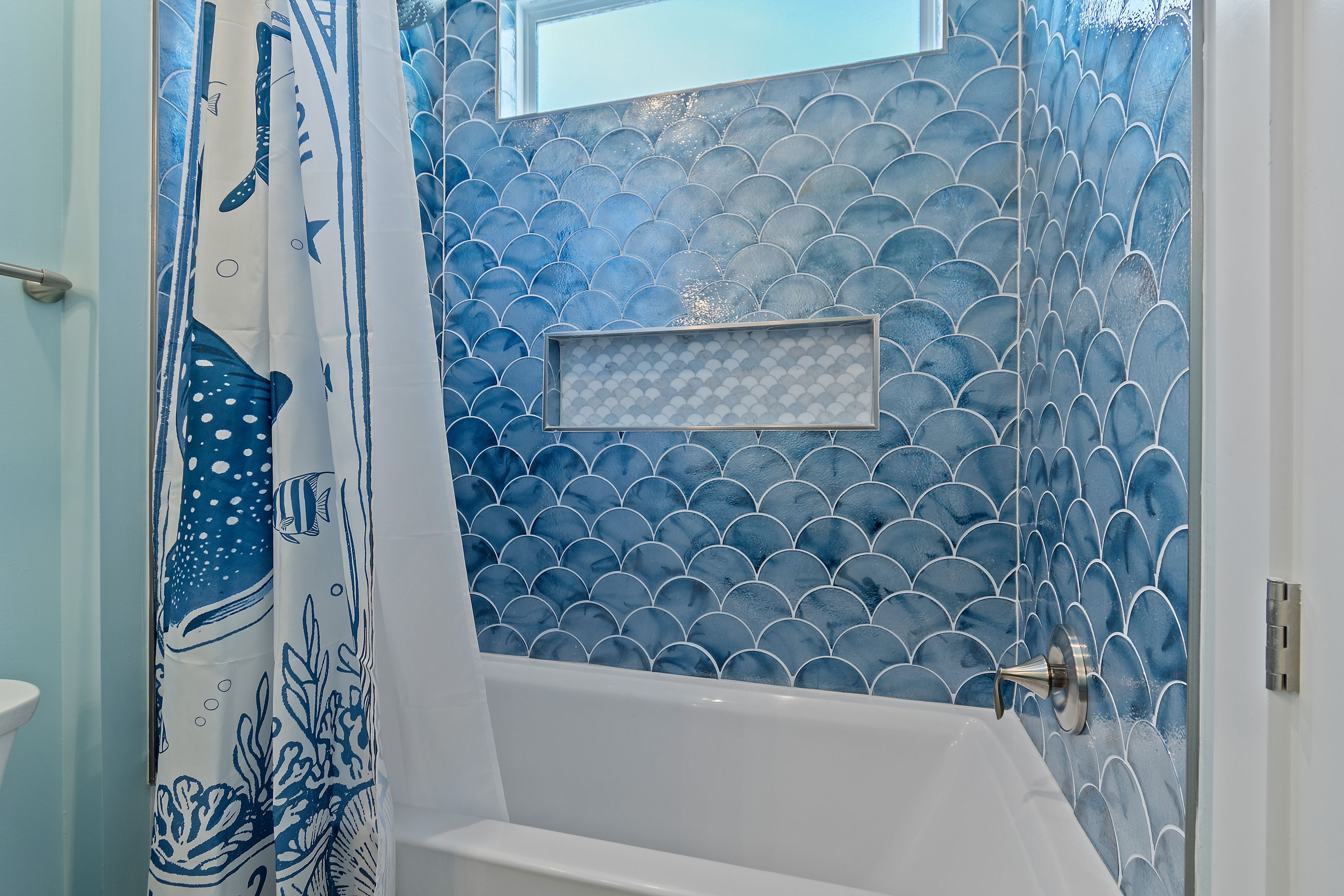 Une salle de bain avec une baignoire, un rideau de douche à motifs bleus et blancs, et un mur orné de carreaux bleus.