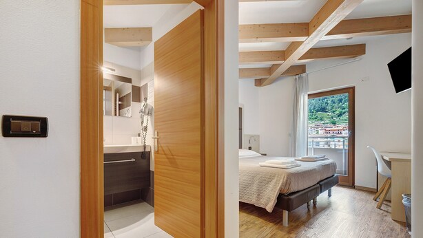 A bedroom with a bed, a desk, and a view of a green landscape through a window.