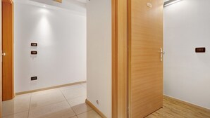 A hallway with a wooden door, white walls, and a tiled floor.