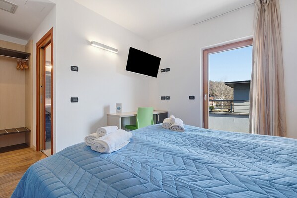A hotel room with a bed, a TV mounted on the wall, a desk with a chair, and a view through a door. - Room 'Camera Matrimoniale' with Mountain View, Wi-Fi and Air Conditioning (Mori)